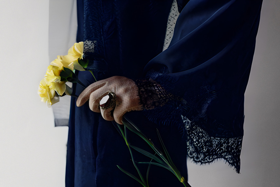 Woman wearing long sleeves and gloves attending a cremation service and holding a yellow rose.