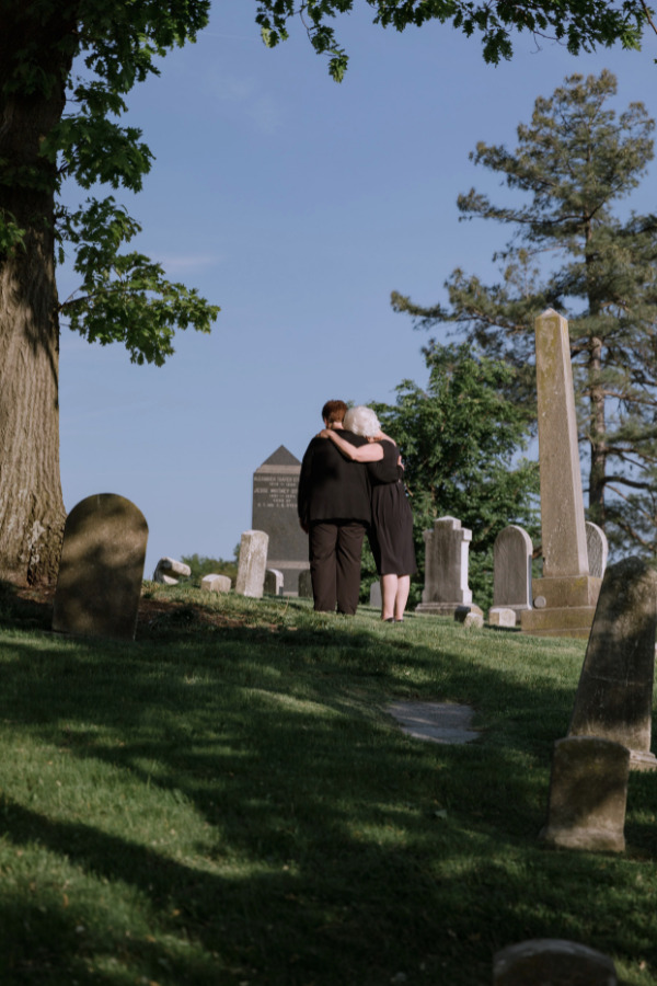 Family members holding each other while looking over their loved ones grave.