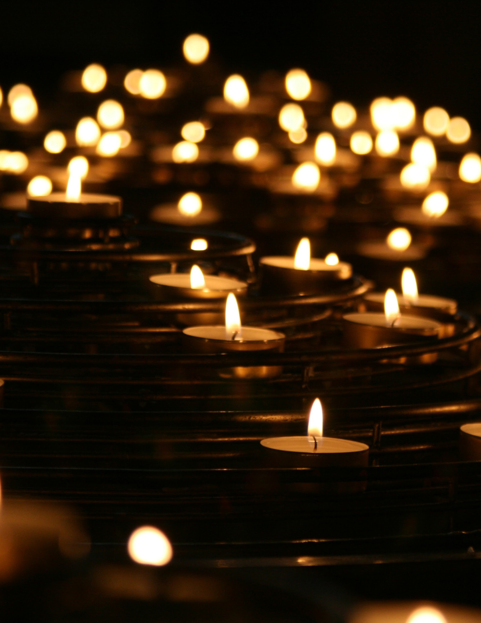 Dozens of lit tea lights in a dark environment.