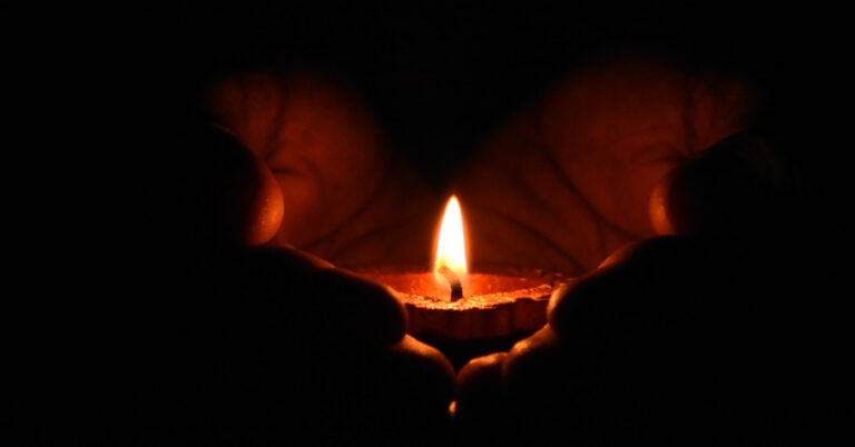 A pair of hands holding a lit tea light.
