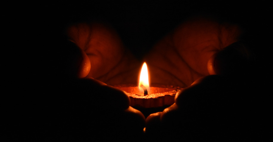 A pair of hands holding a lit tea light.