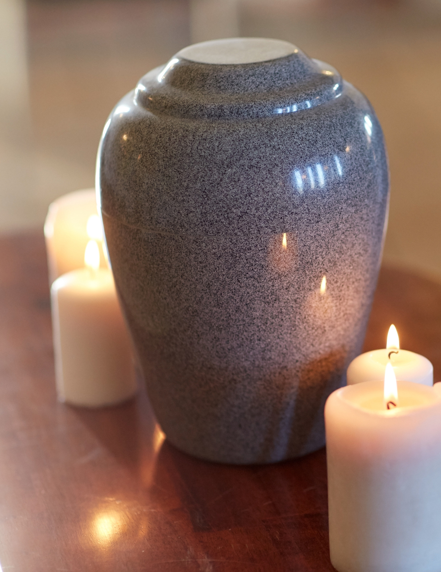 A stone urn on a wood table surrounded by lit candles.