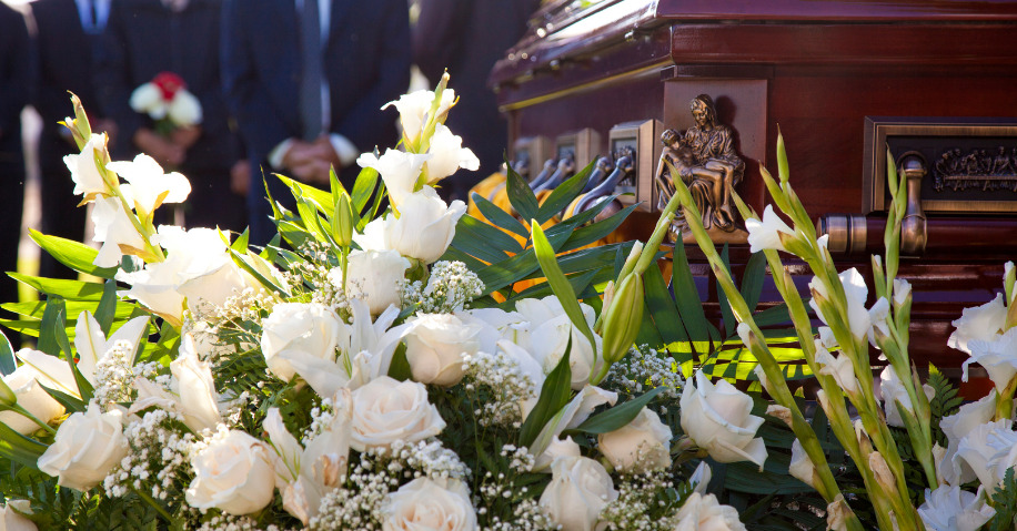 A bouquet of white flowers in front of a coffin and funeral attendees.