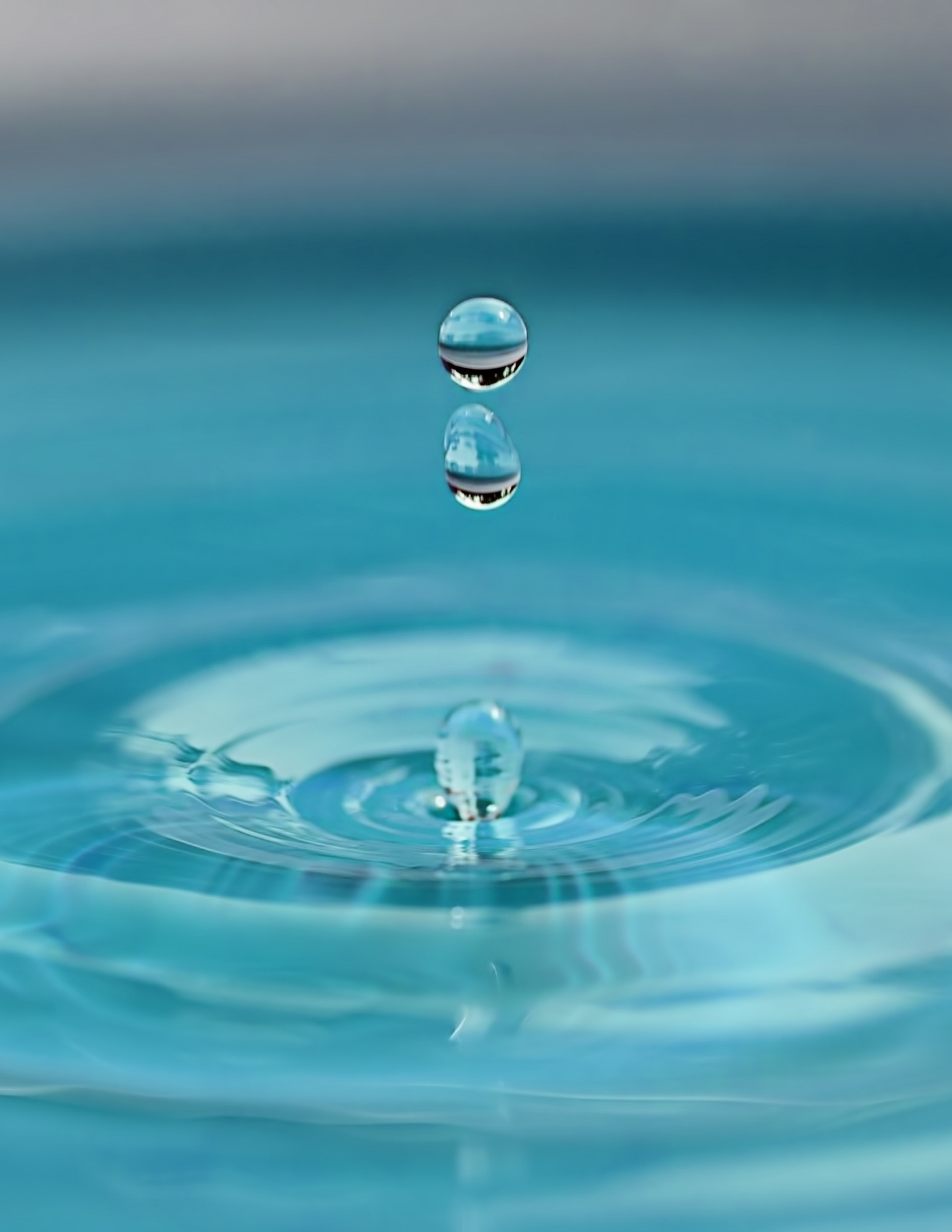 Three droplets of water falling into clear blue water, causing ripples.