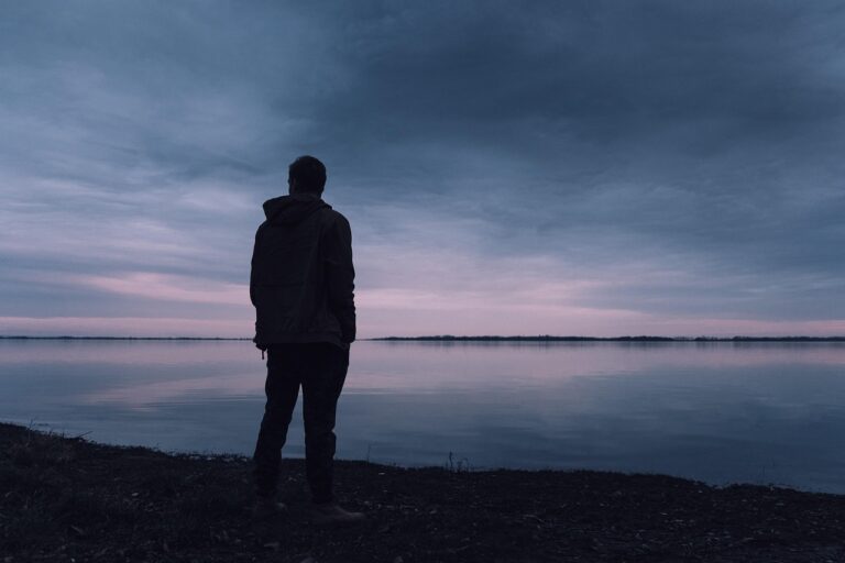 a man standing alone on the shore of a lake