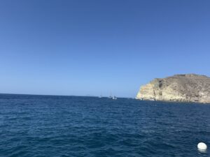 Ocean horizon with boats in the distance and a rocky coastline to the right.