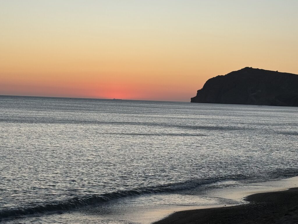 Calm ocean sunset behind cliff