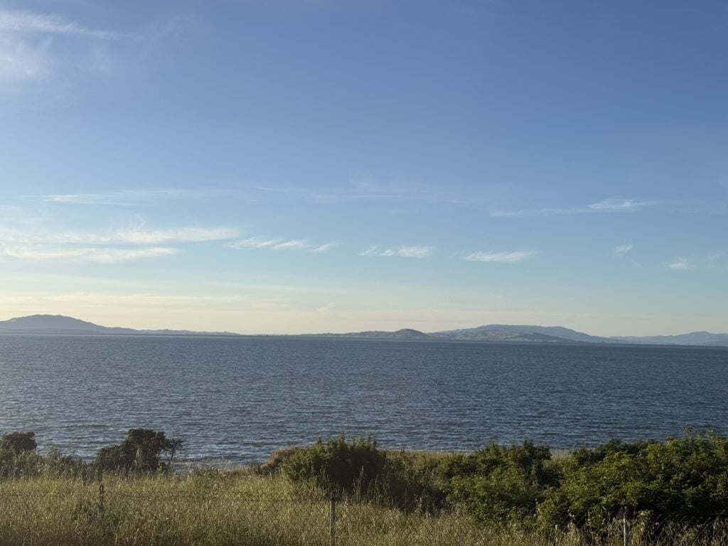 A calm coastal view with blue water, distant mountains, and a clear sky.