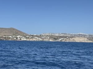 A calm ocean view with deep blue water, a clear sky, and a distant hillside town along the shore.
