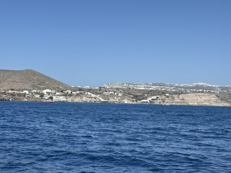 A calm ocean view with deep blue water, a clear sky, and a distant hillside town along the shore.