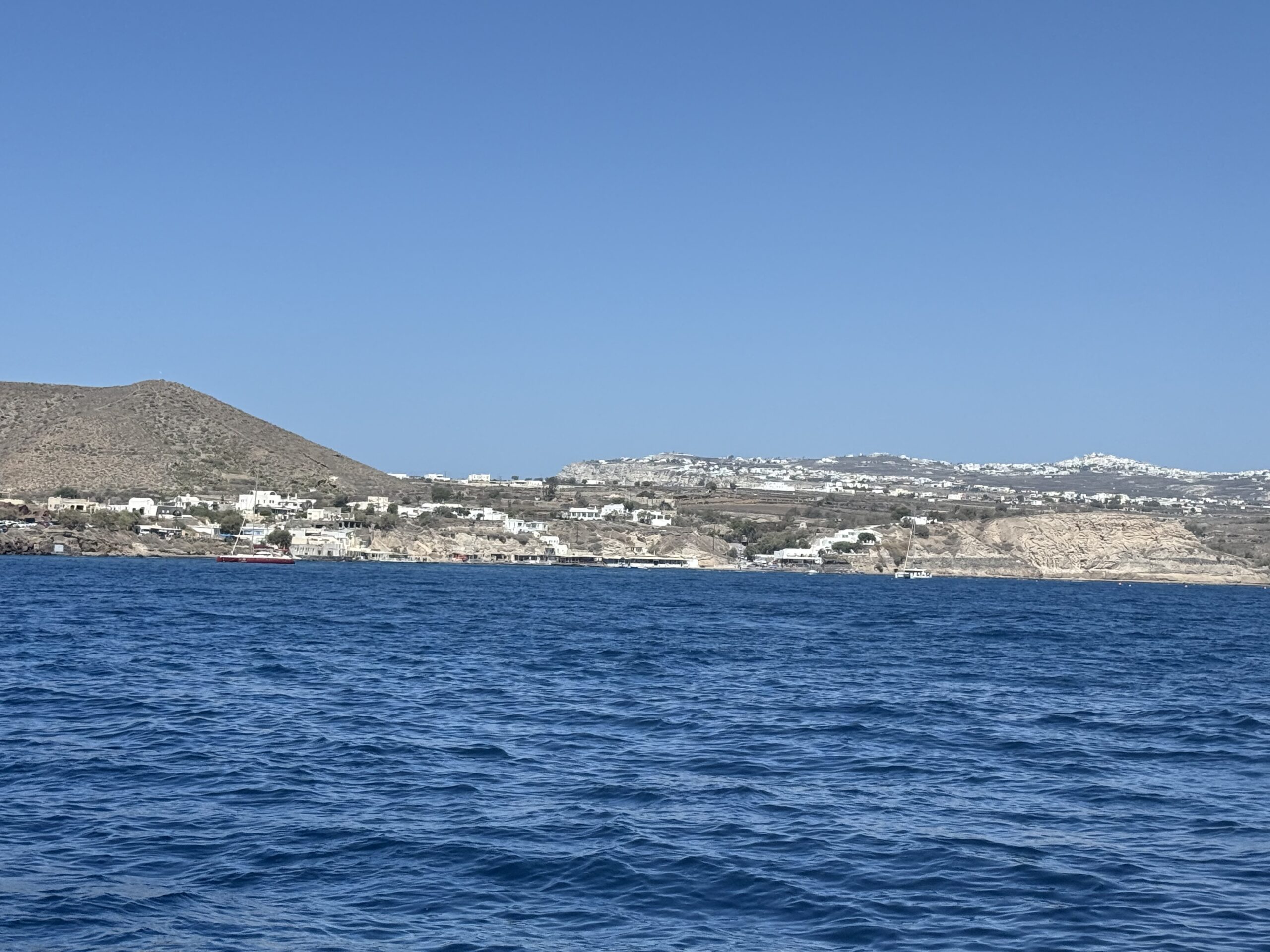 A calm ocean view with deep blue water, a clear sky, and a distant hillside town along the shore.