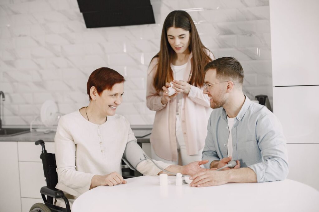A woman in a wheelchair smiles while two family members help organize her medication at home