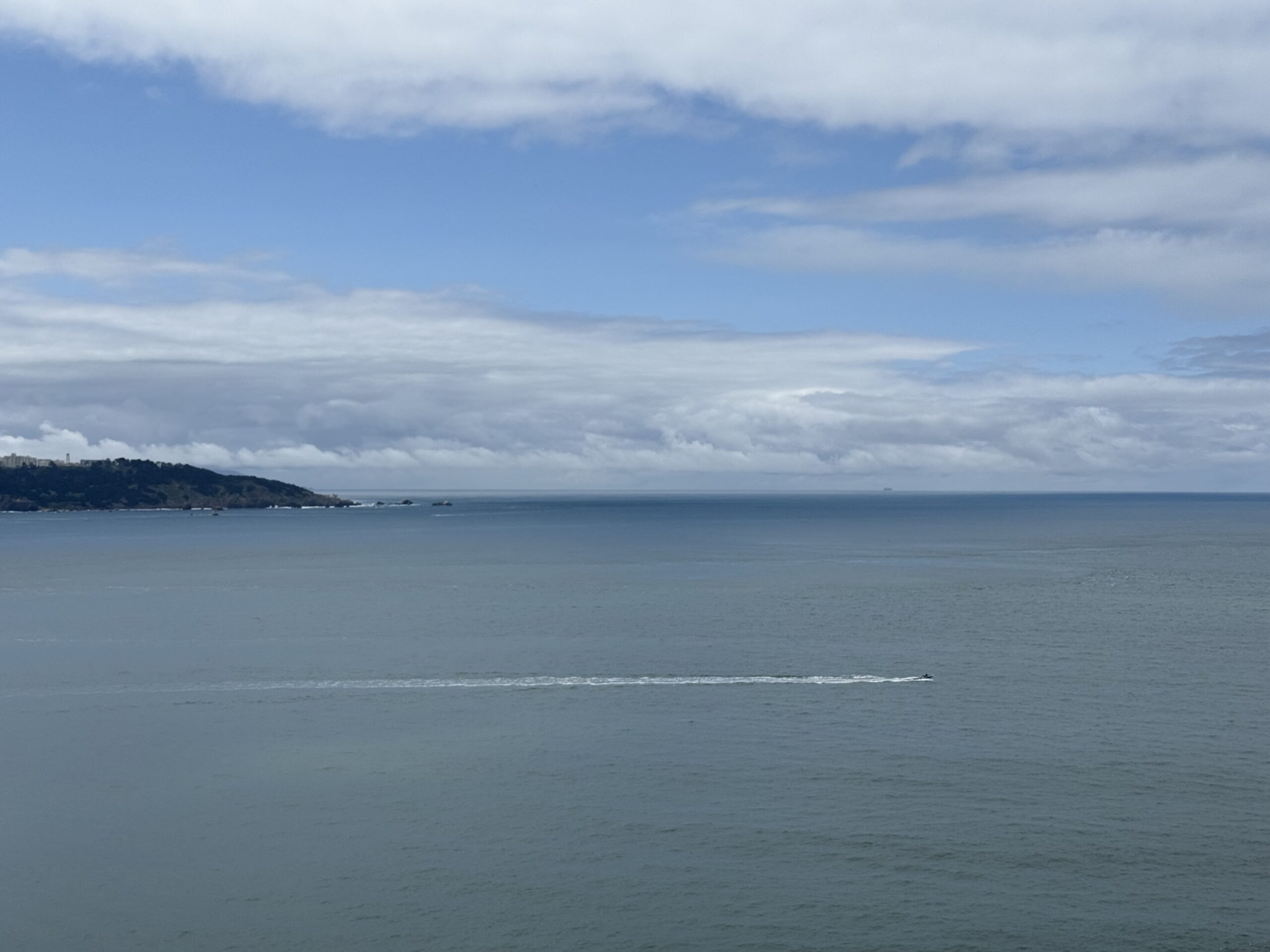 A calm ocean beneath a cloudy sky, with a distant coastline on the horizon