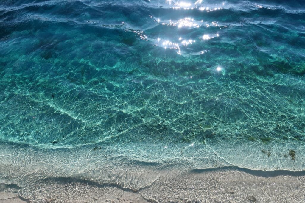 Clear turquoise ocean water gently meeting a sandy shore in bright sunlight.
