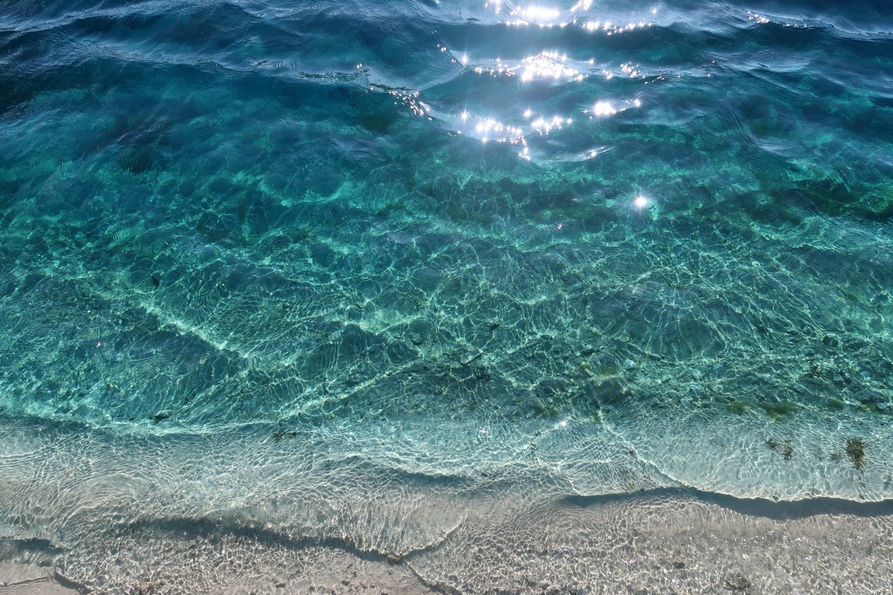 Clear turquoise ocean water gently meeting a sandy shore in bright sunlight.