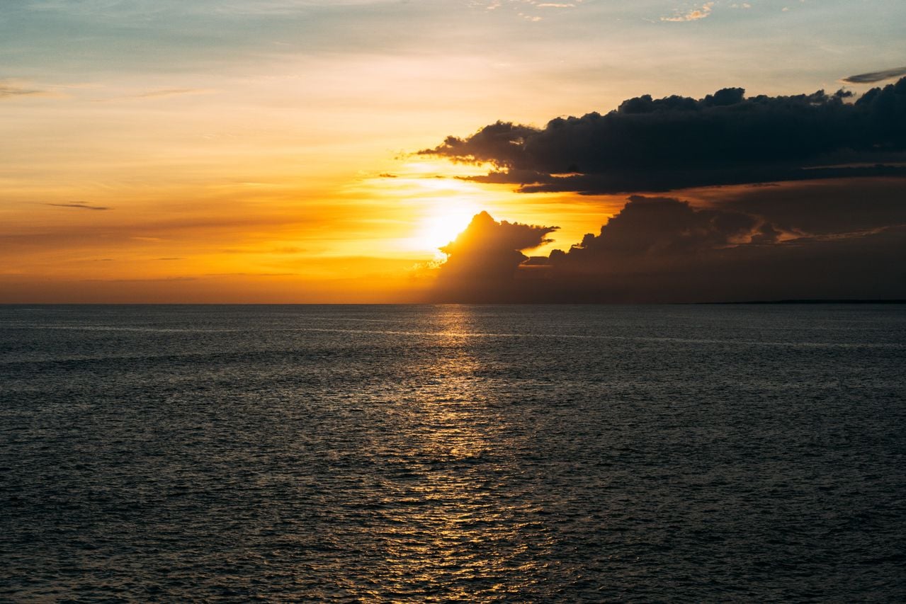 A golden sunset over the ocean, with dramatic clouds and sunlight reflecting across the water.
