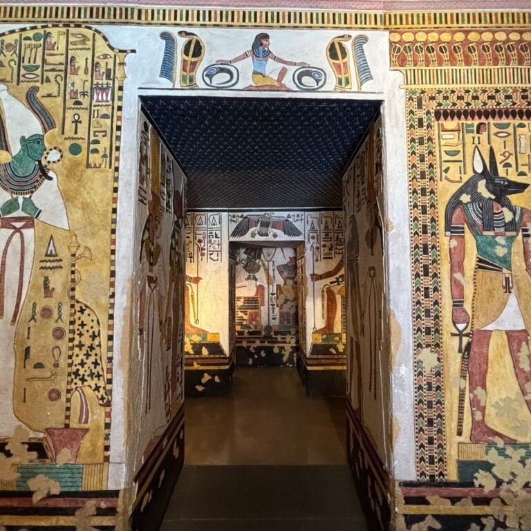 An ancient Egyptian tomb interior decorated with colorful hieroglyphs and wall paintings, including a prominent image of Anubis with a jackal head.