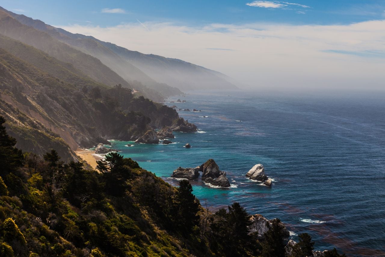 A peaceful coastal landscape with rugged cliffs, blue ocean water, and misty mountains in the distance.
