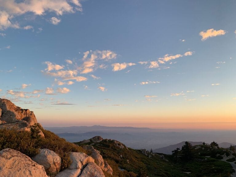 A rocky mountain landscape under a soft blue sky with warm sunset light on the horizon.
