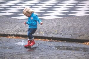 A child in red rain boots splashing through a puddle on a rainy day.