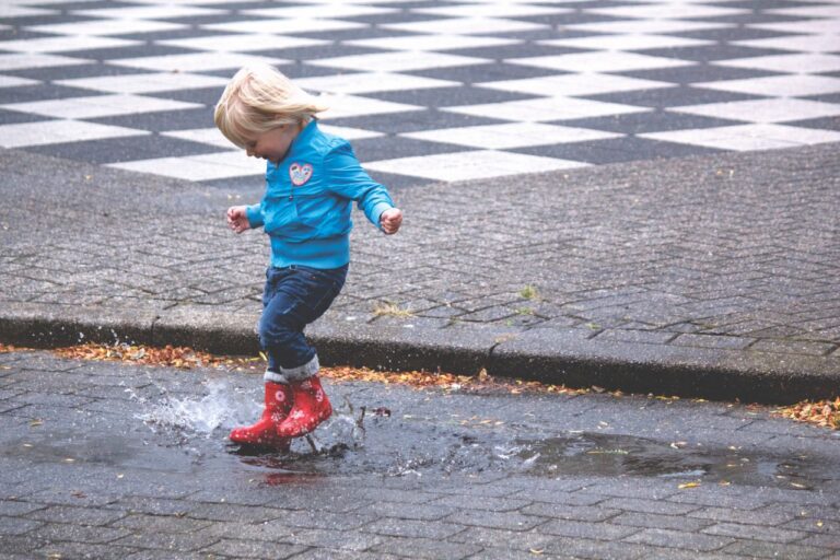 A child in red rain boots splashing through a puddle on a rainy day.