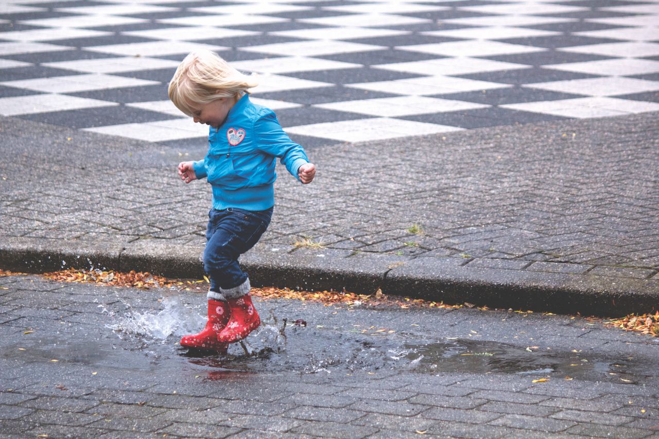 A child in red rain boots splashing through a puddle on a rainy day.