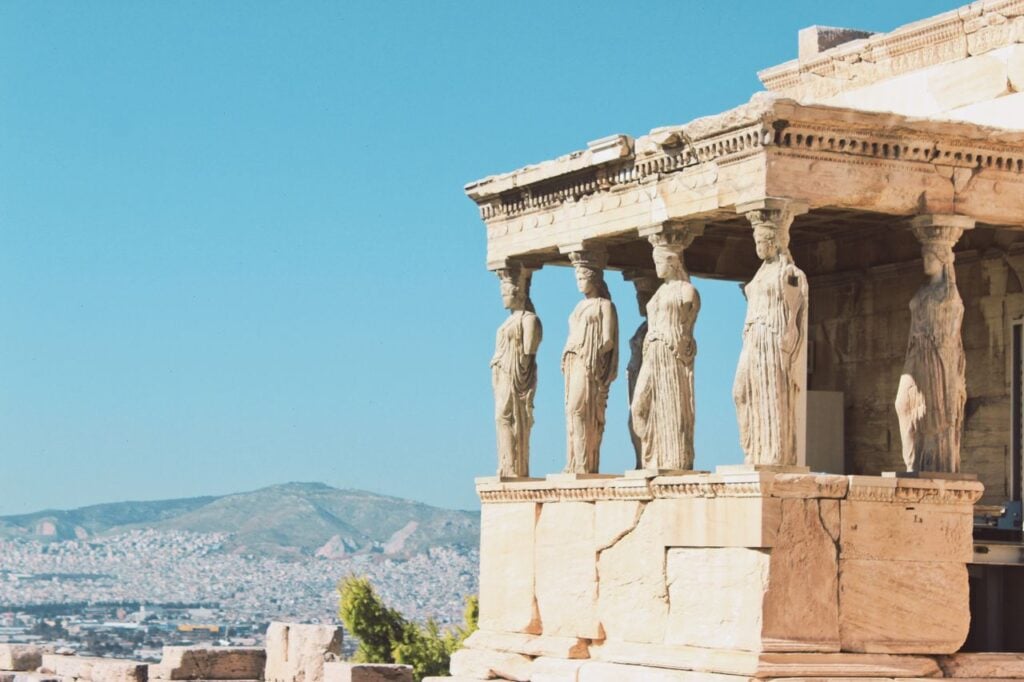 Ancient Greek ruins with Caryatid statues overlooking Athens under a clear blue sky.