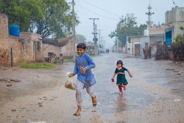 Two children running and playing on a wet street during the rain.