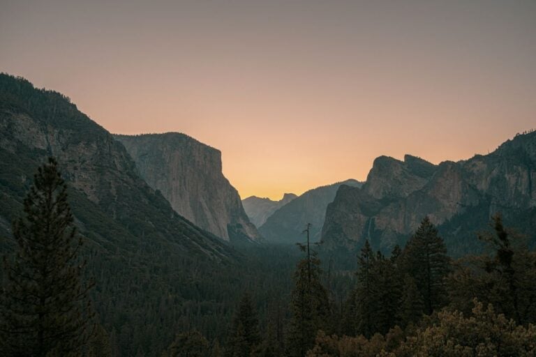 A peaceful mountain valley at sunset, with soft golden light glowing between the peaks.