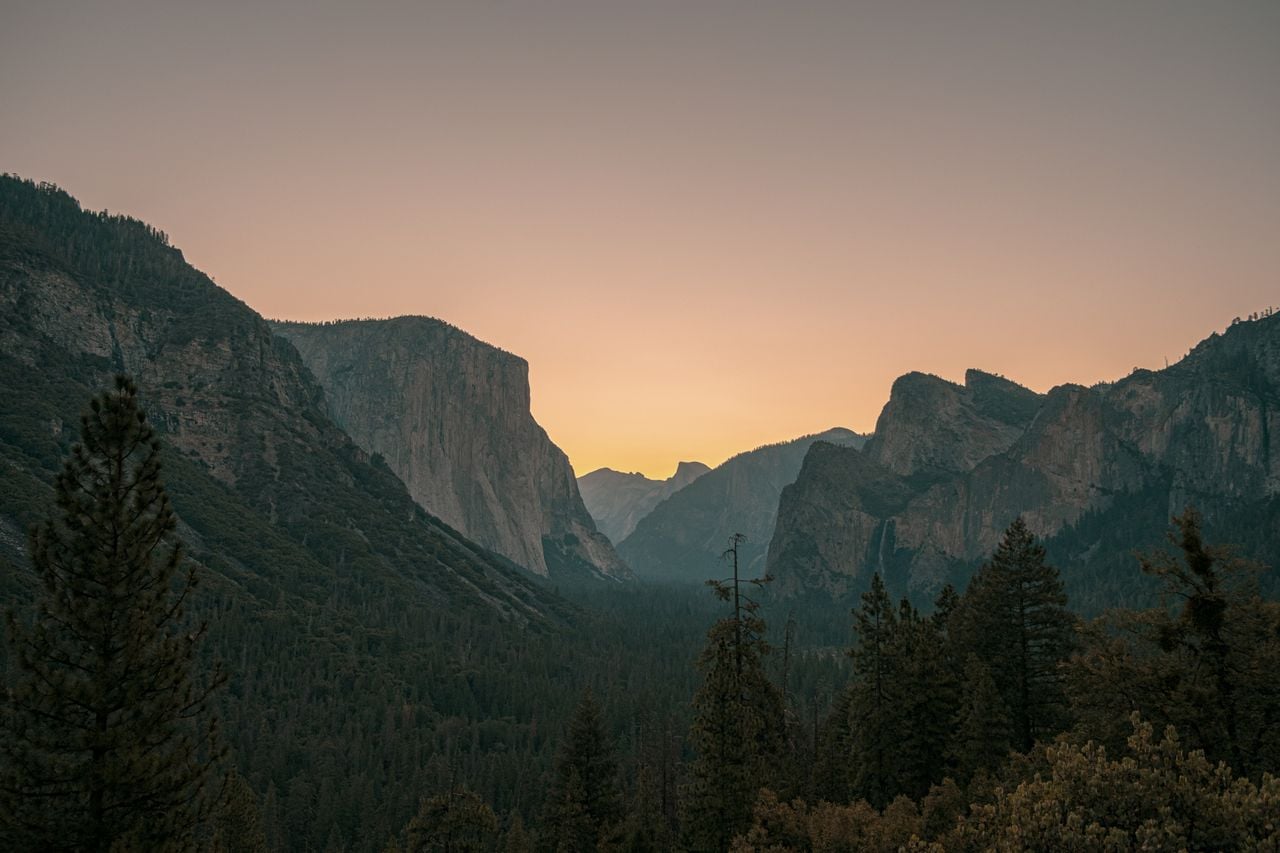 A peaceful mountain valley at sunset, with soft golden light glowing between the peaks.