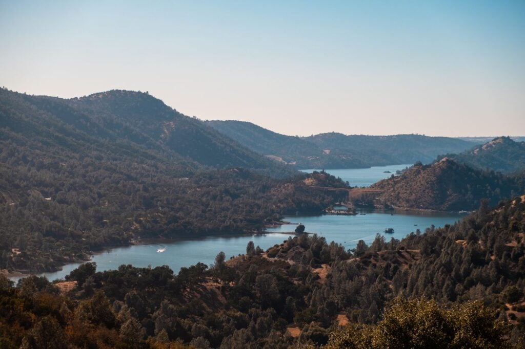 A scenic lake nestled between forested hills and mountains, under a clear blue sky.